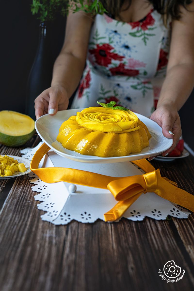 a female holding a mango pudding plate with a half cut mango on the side