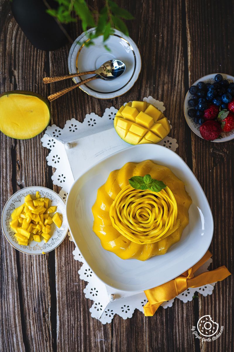 overhead shot of mango pudding in a white plate with some chopped mangoes and a half mango kept on the side