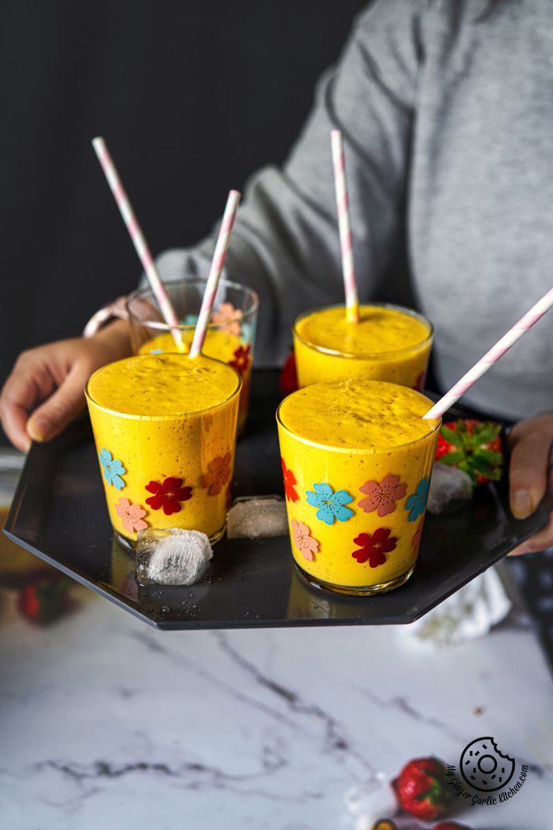 a female holding a tray with 4 glasses filled with mango smoothie