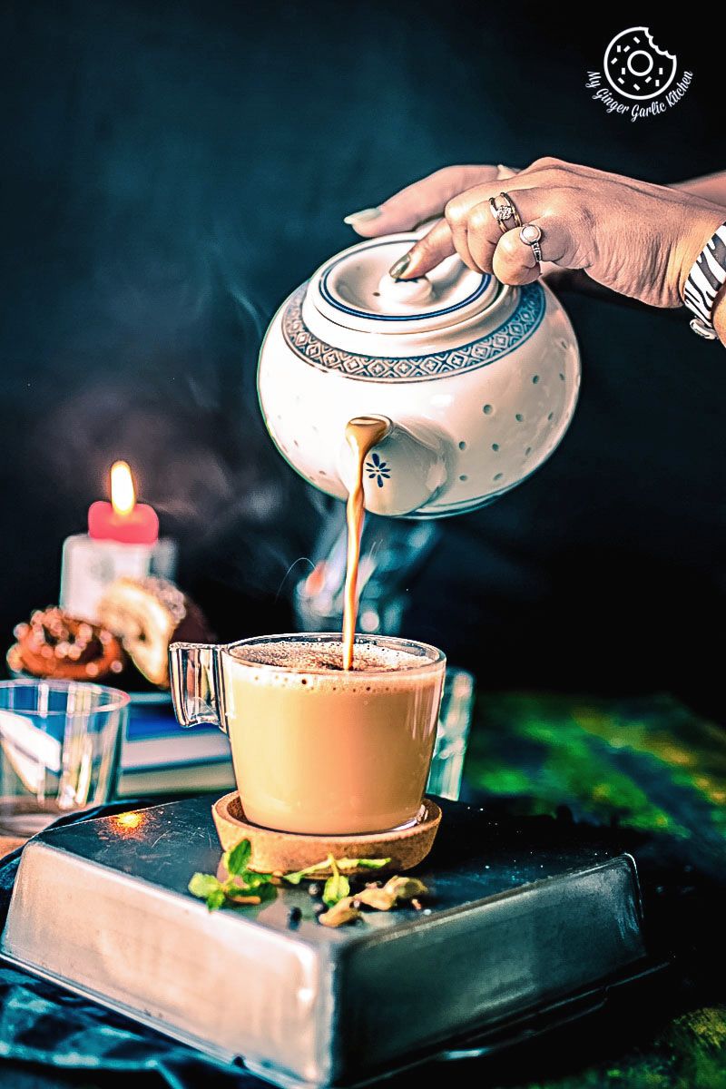 someone pouring masala into a cup on a table with some spices and candle in background