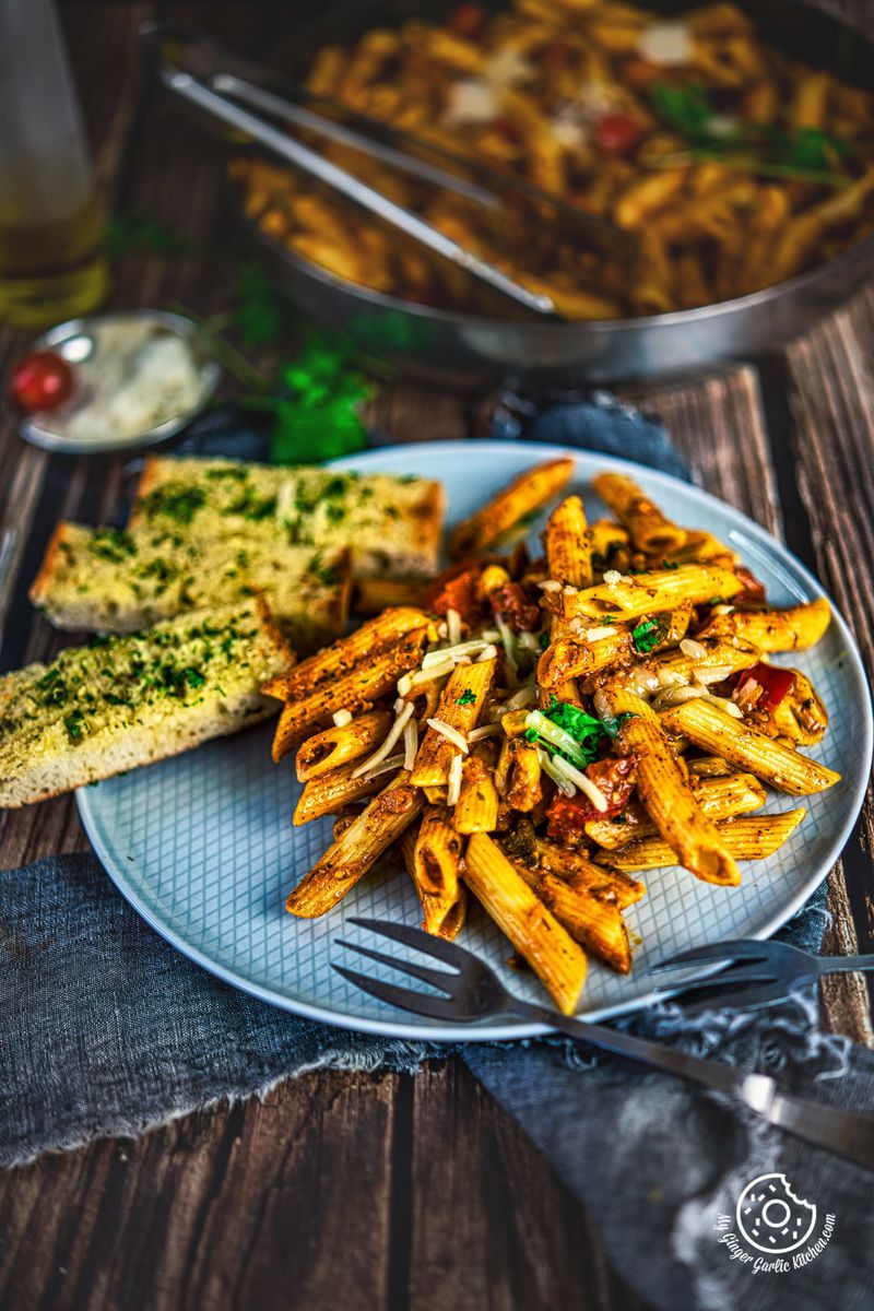 masala pasta served in a grey plate along with garlic bread sticks