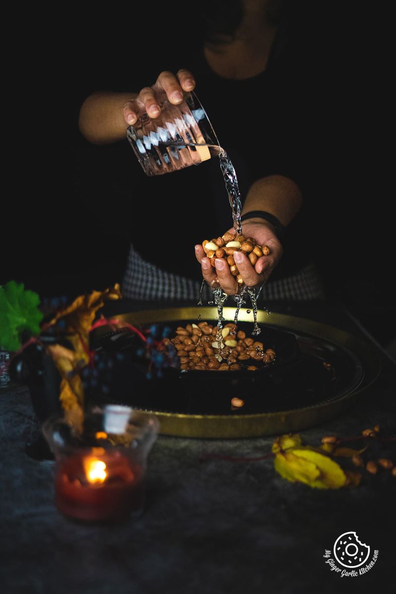 Pouring water over a handful of masala peanuts with a mystical dark ambiance, candlelight, and autumn leaves.