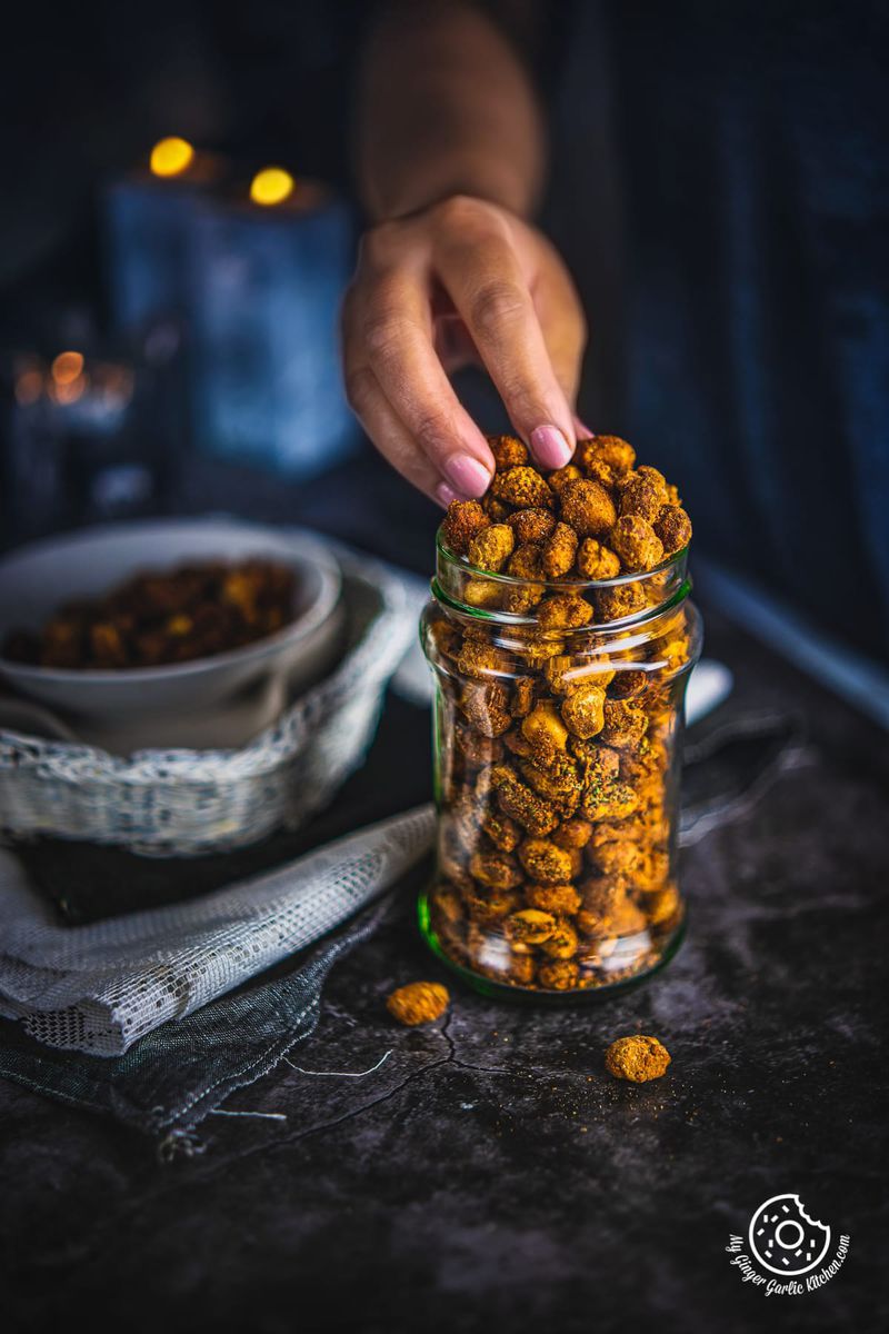 a hand picking masala peanut from a transparent jar