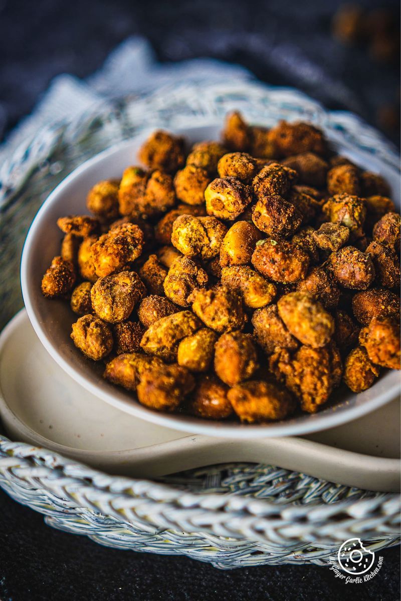 Close-up of spiced masala peanuts piled in a white ceramic bowl on a dark fabric surface with a lace underlay.