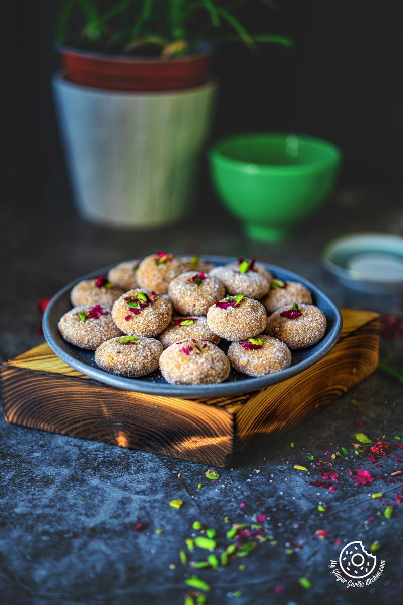 there is a plate of mathura pedas with chopped pistachios and dried rose petals on a table