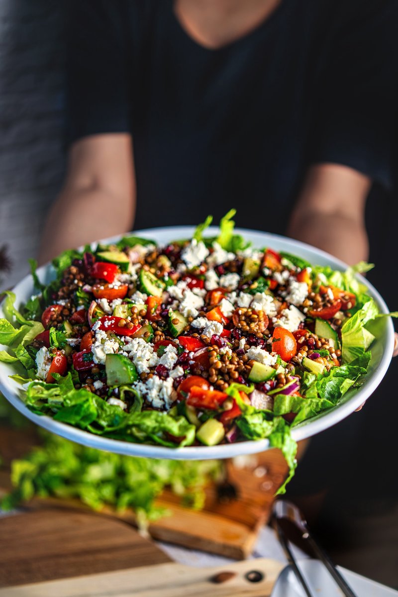 Mediterranean lentil salad with feta, pomegranate, cucumber, tomatoes, and fresh herbs served on romaine lettuce