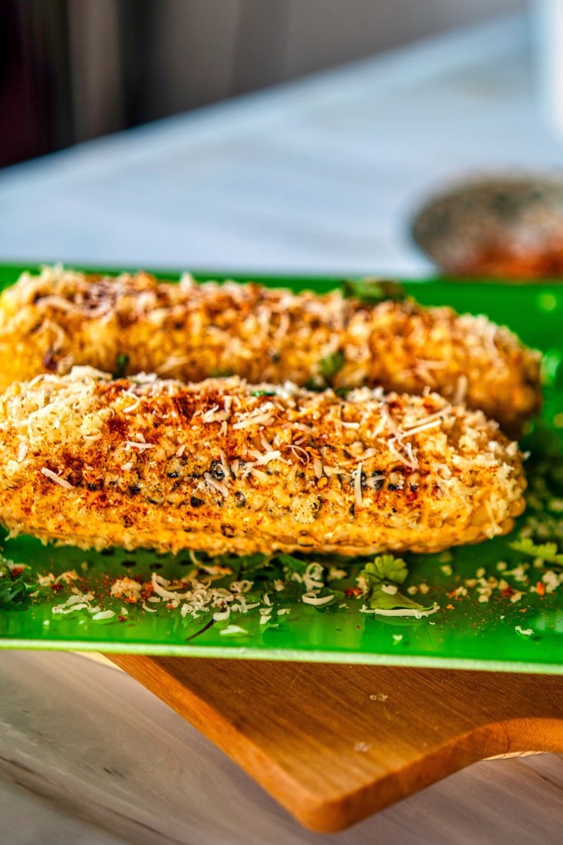 Mexican street corn recipe with two grilled elotes topped with creamy garlic-lime sauce, feta, chili, cilantro, and fresh lime