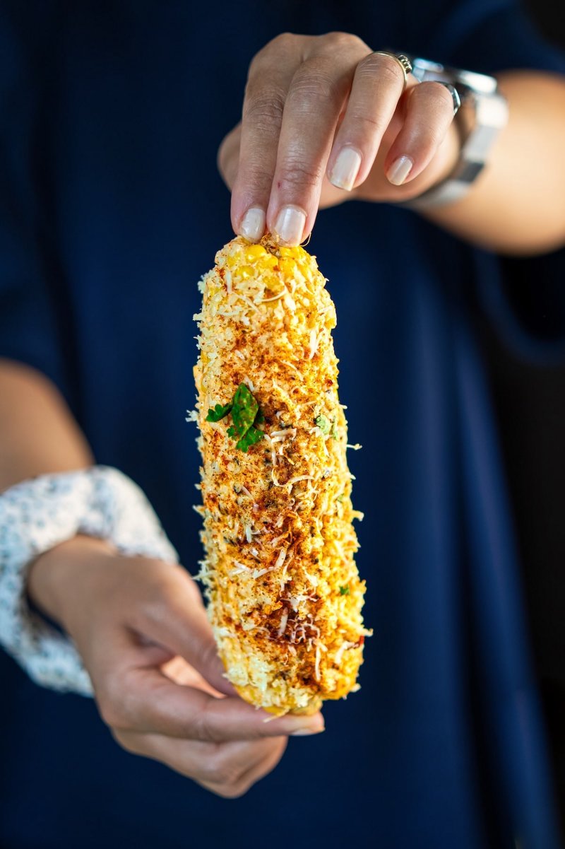 Close-up of Mexican street corn with charred kernels, creamy garlic-lime sauce, grated feta, chili, and fresh cilantro