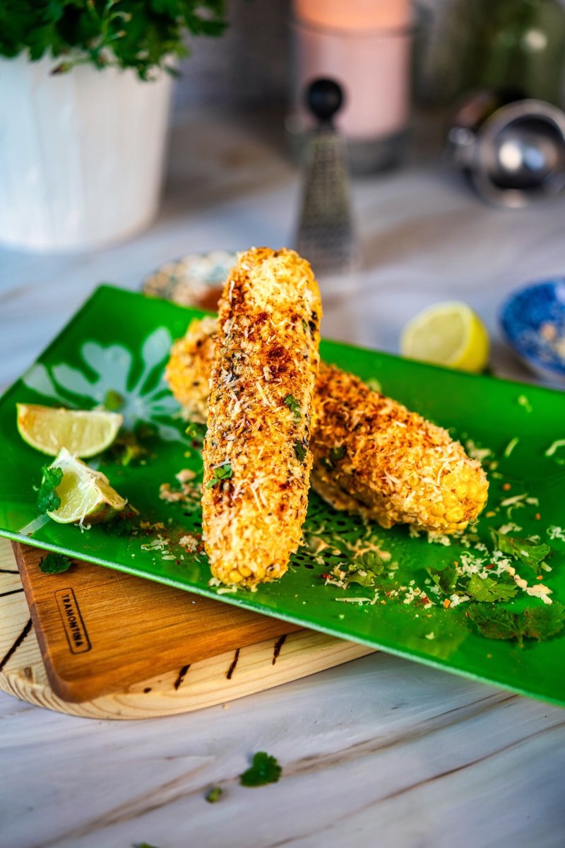 Grilled Mexican street corn topped with creamy sauce, grated feta, chili seasoning, and cilantro on a green plate