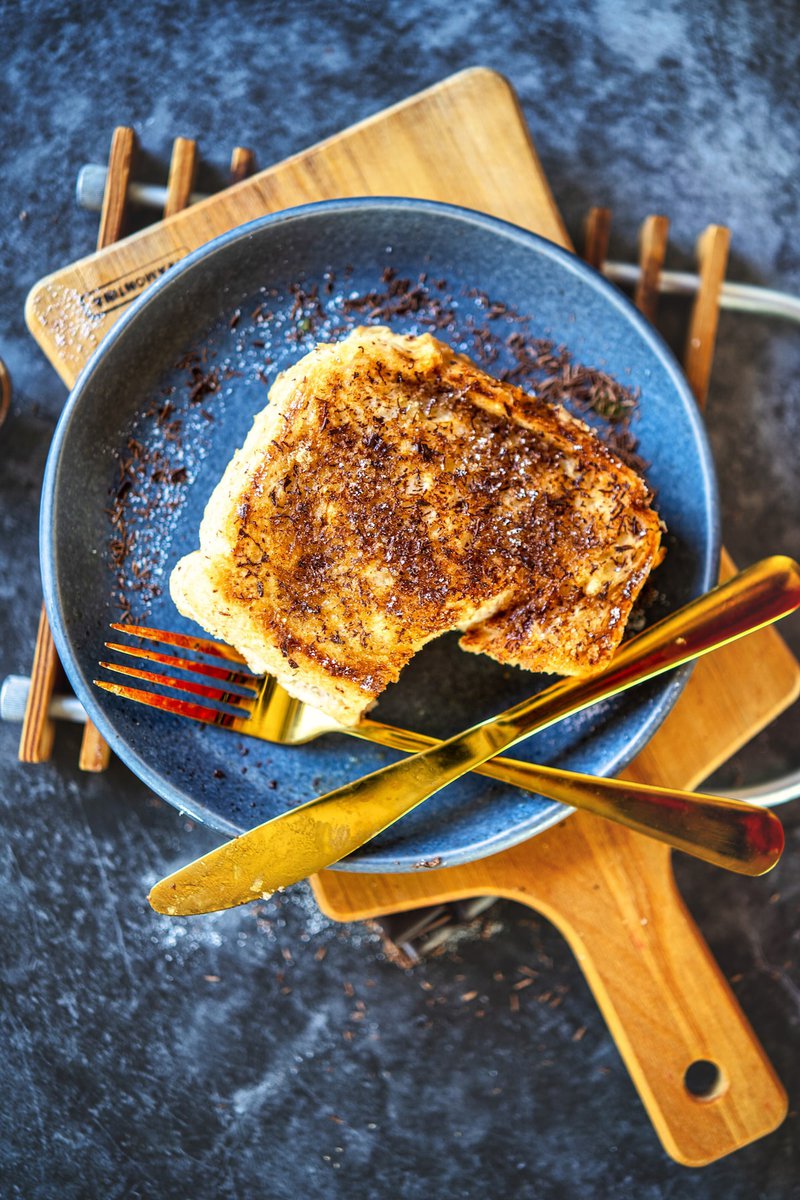 Golden-brown milk toast on a grey plate with golden utensils, atop a wooden cutting board.