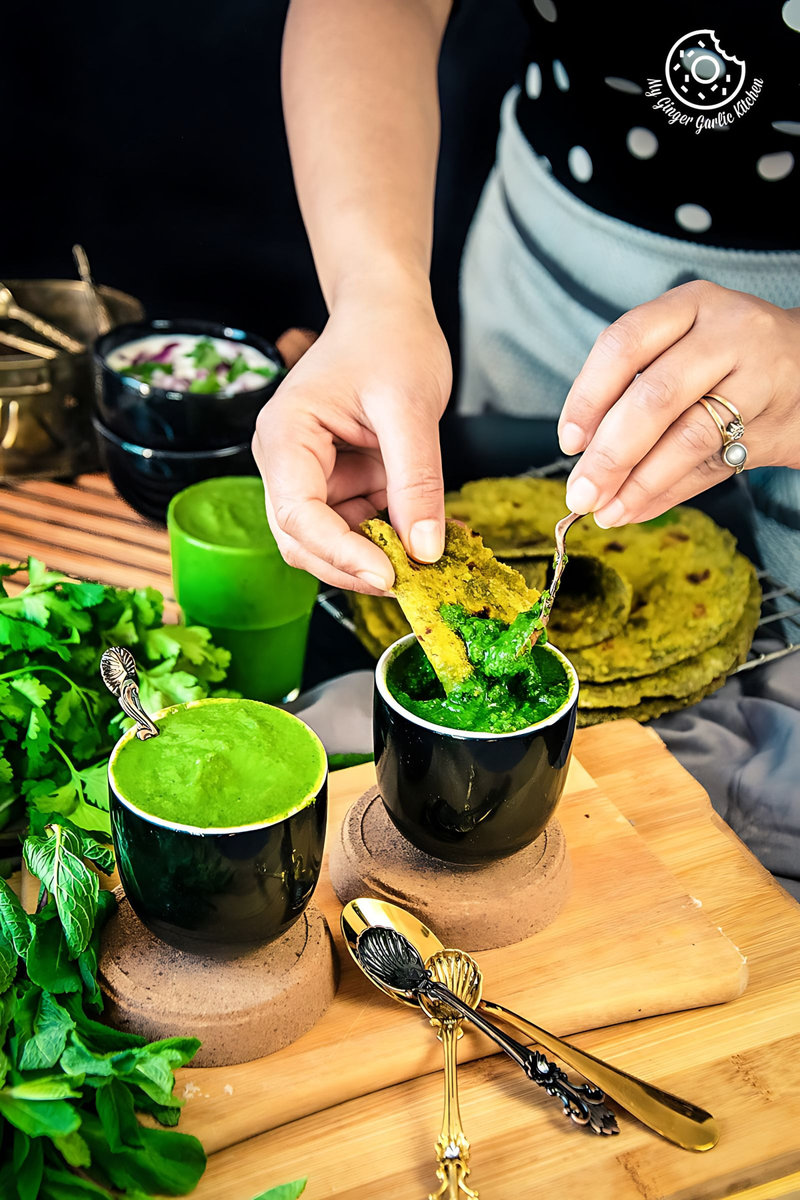a female dipping flatbread into mint coriander chutneys served in a black ceramic bowl