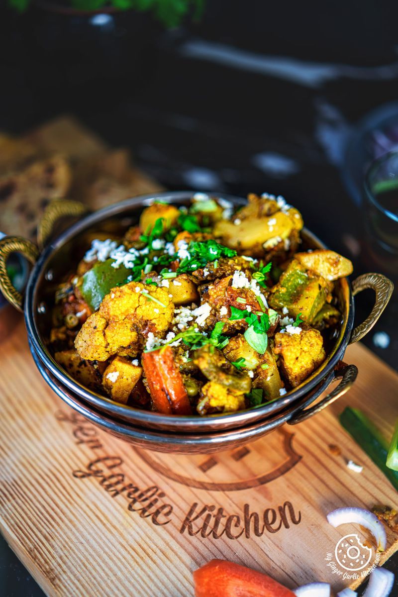 closeup of mix veg garnished with coriander and grated paneer in a copper kadai
