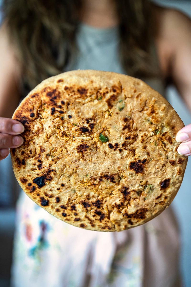 A person holding a freshly cooked Mooli Paratha (Radish Paratha), showcasing its golden-brown surface.