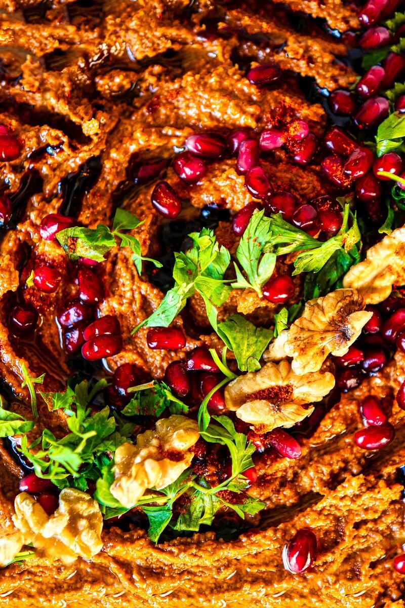 Close-up of richly textured Muhammara dip topped with fresh pomegranate seeds, chopped parsley, and crunchy walnuts