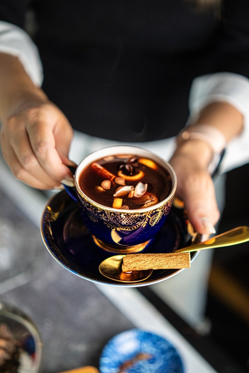 Holiday spiced berry juice served in a blue cup with cinnamon stick, star anise, orange peel, and almond flakes, a cozy non-alcoholic mulled berry juice recipe