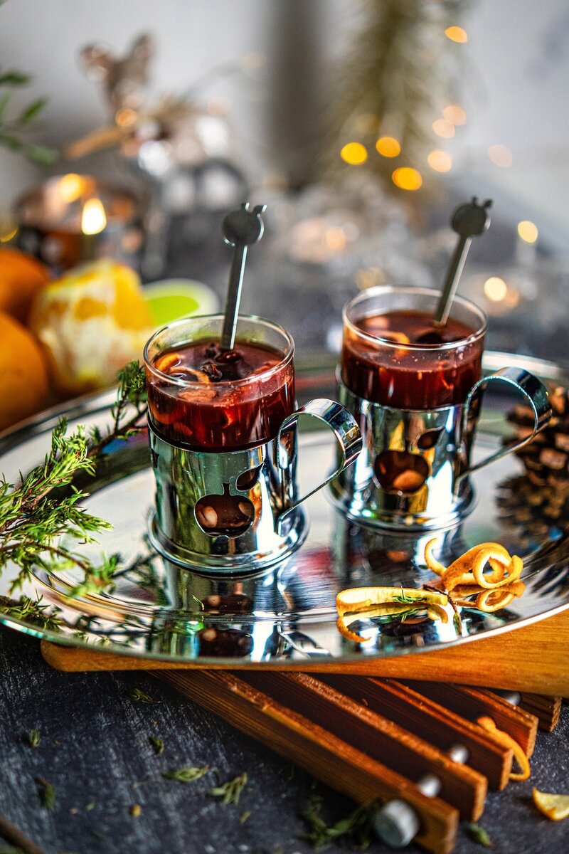 Two glasses of holiday spiced berry juice garnished with cinnamon sticks, star anise, and orange peel, non-alcoholic mulled berry juice recipe