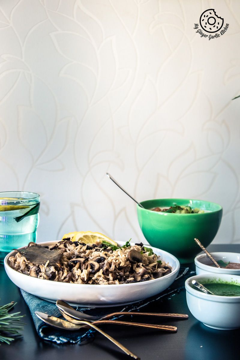 a plate of mushroom pulao on a table with bowls of chutneys and raitas