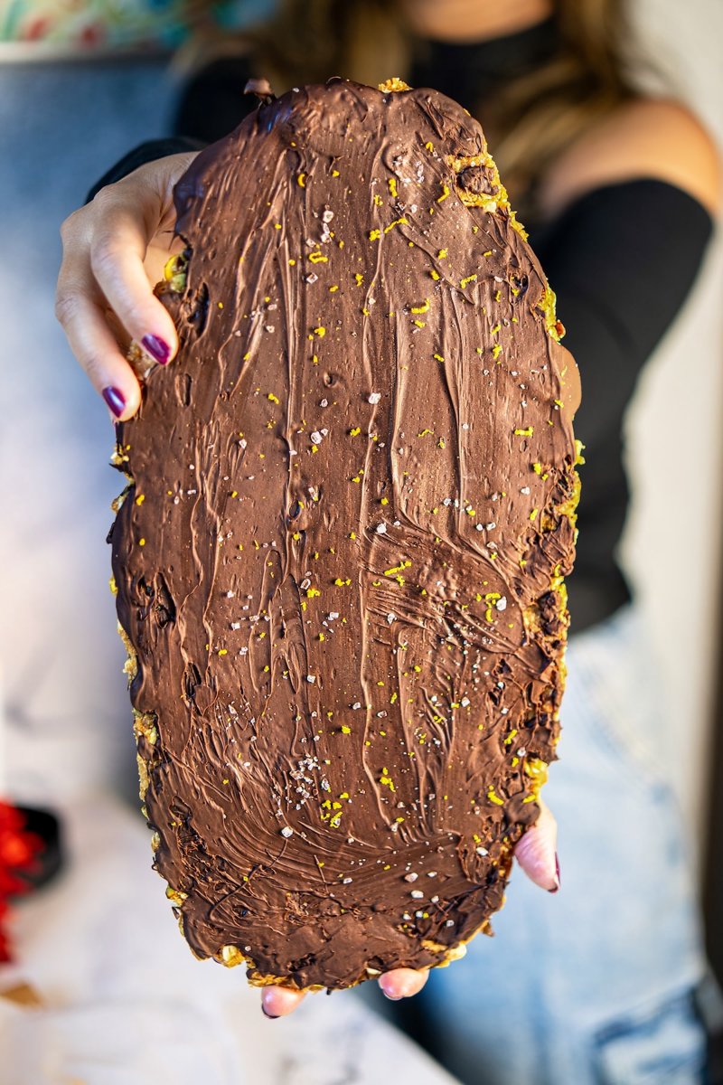 Chocolate-covered no-bake almond energy bars held in both hands, topped with orange zest and flaky sea salt.