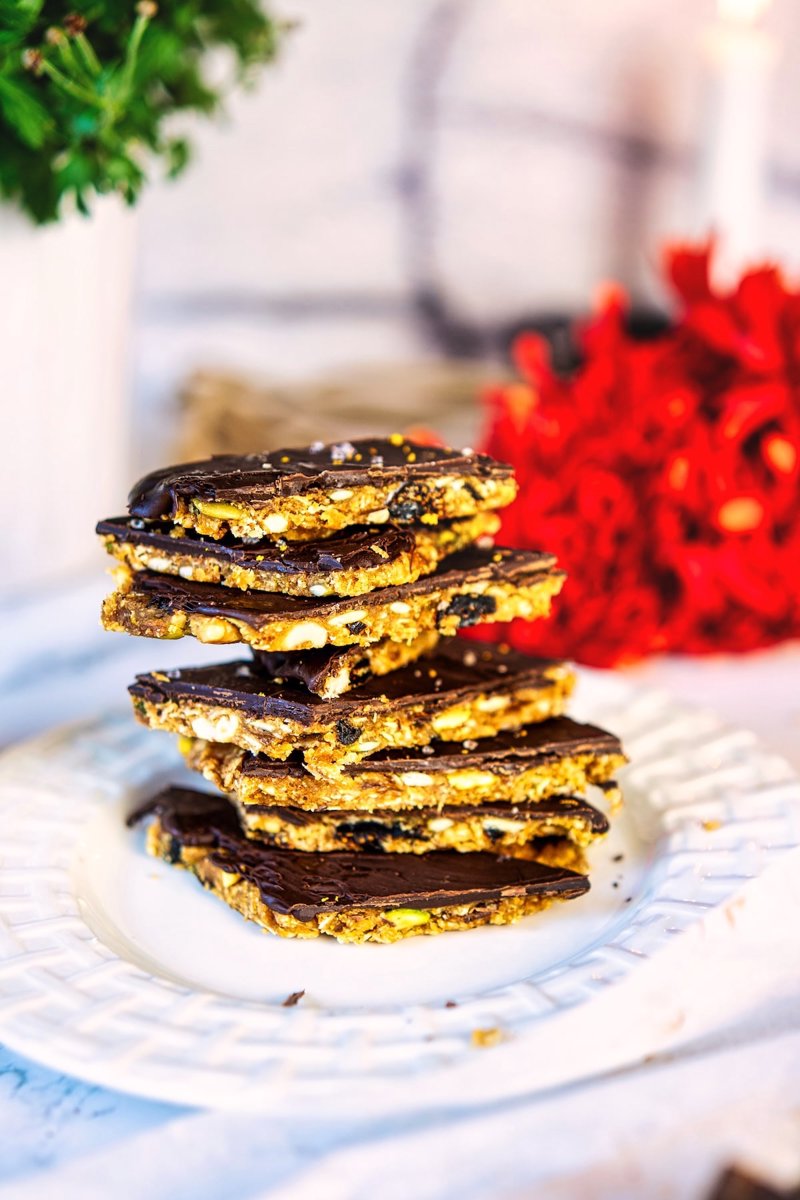 Stack of chocolate-covered no-bake almond energy bars showing the crunchy nuts, seeds, and dried fruit filling.