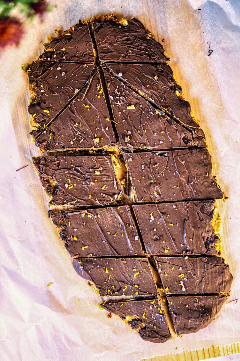 No-bake almond energy bars sliced into triangles and rectangles with a dark chocolate topping, orange zest, and flaky sea salt.