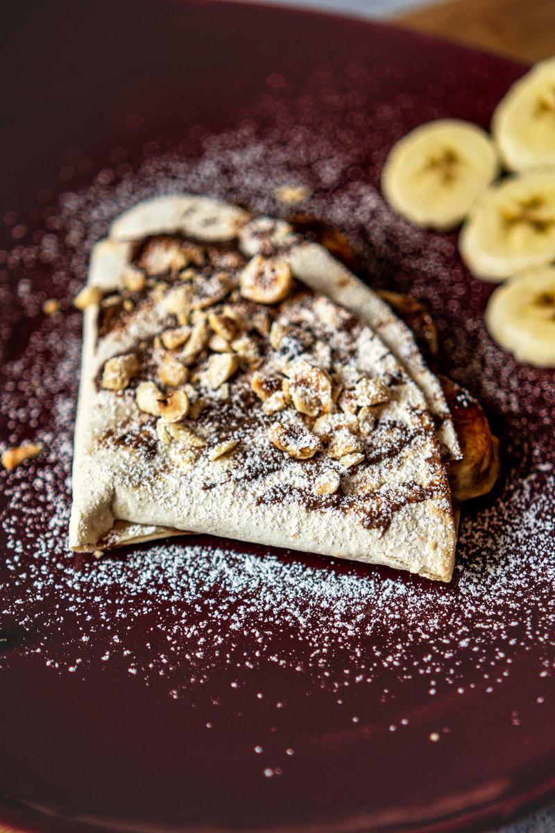 Nutella Banana Wrap filled with banana and nuts, dusted with powdered sugar on a dark red plate.