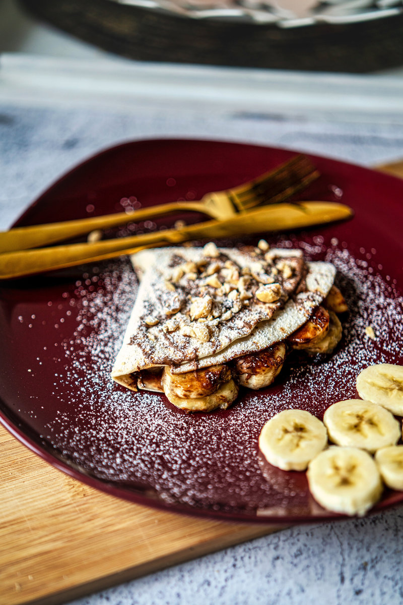 Close-up of a nutella banana tortilla wrap with caramelized bananas and nuts on a burgundy plate.