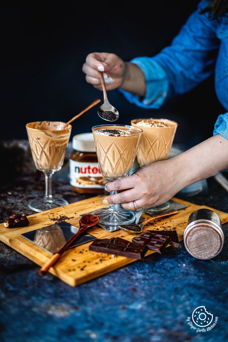 a female holding a chocolate srpinkle spoon over a nutella mousse glass