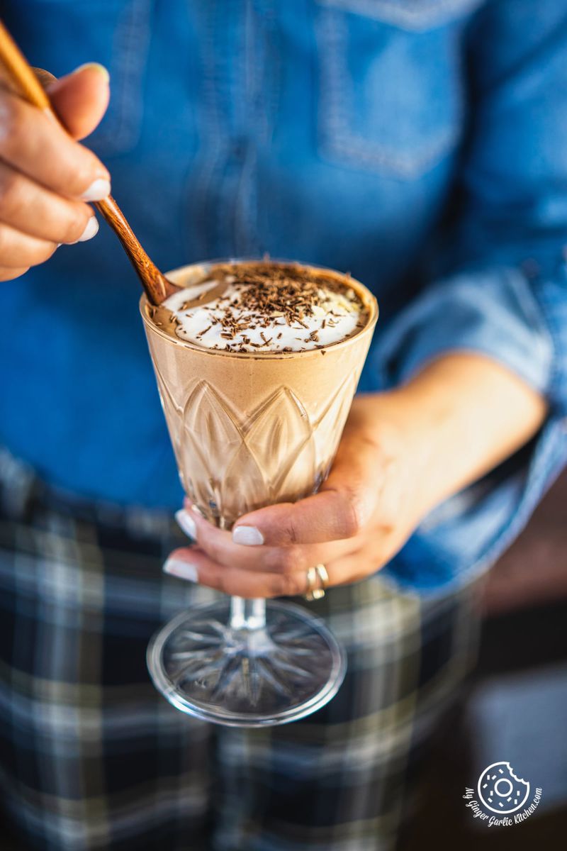 a female holding a nutella glass topped with whipped cream and chocolate shavings