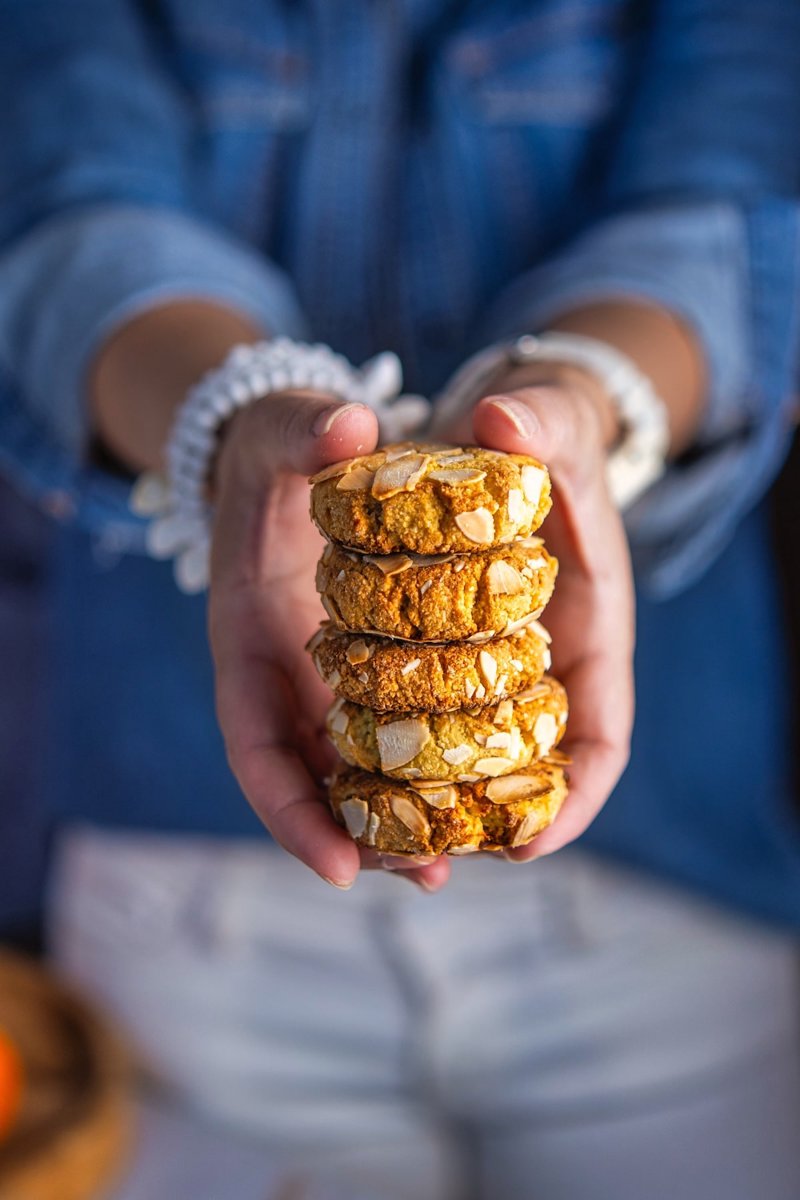 Soft and chewy orange almond cookies made with almond flour, stacked in hands and coated with sliced almonds