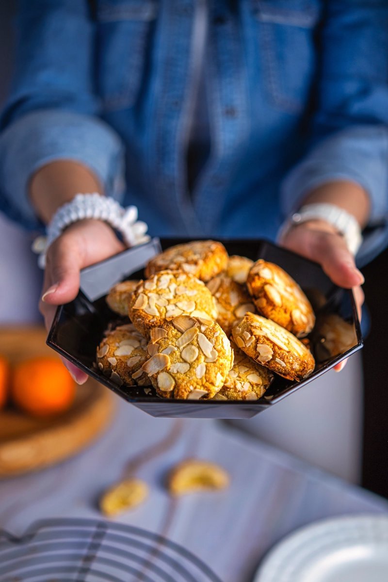 Orange almond cookies made with almond flour and topped with sliced almonds, arranged on a cooling rack beside fresh orange juice