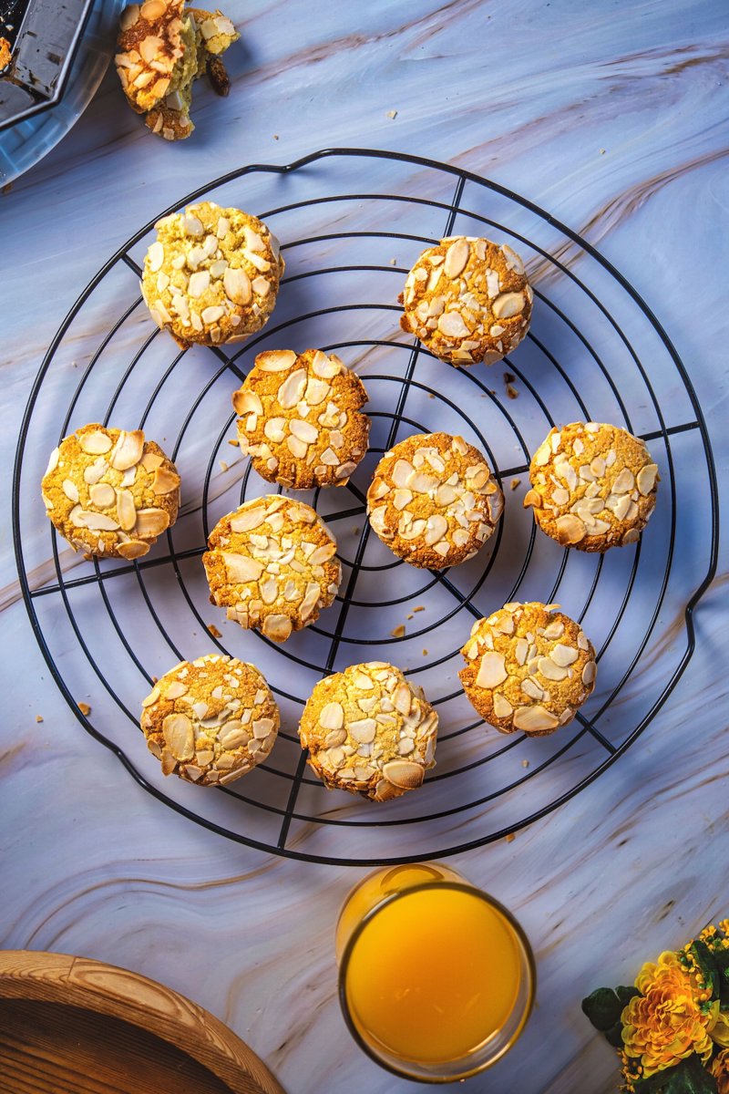 Orange almond cookies made with almond flour and topped with sliced almonds, arranged on a cooling rack beside fresh orange juice