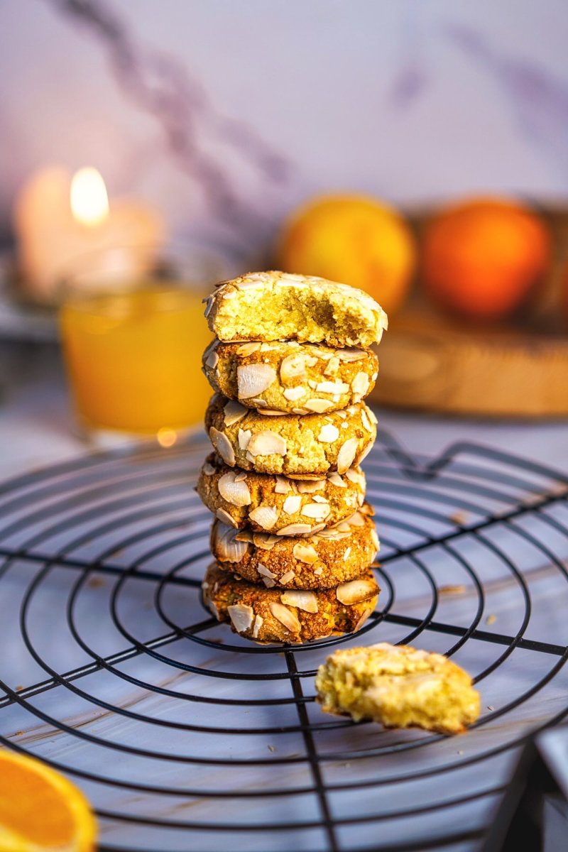 Freshly baked orange almond flour cookies topped with sliced almonds, stacked on a cooling rack with golden edges and soft centers