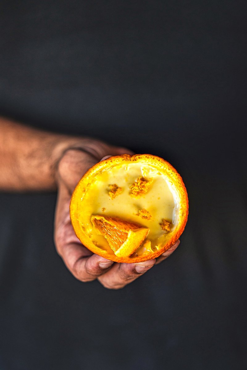 Hand holding a fresh orange posset dessert in an orange shell topped with orange segments and fragrant orange zest.