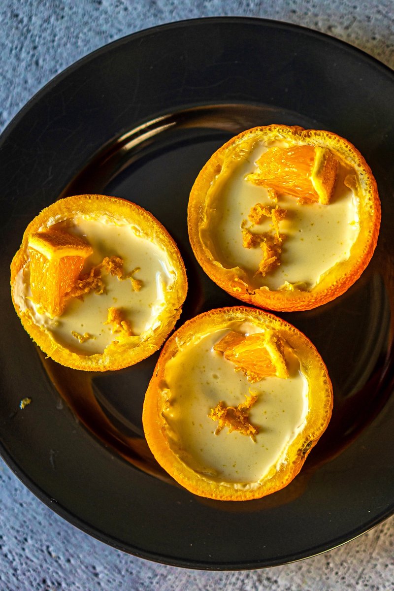 Top view of silky smooth orange posset dessert in hollowed orange peels with fresh orange slices and citrus zest topping.