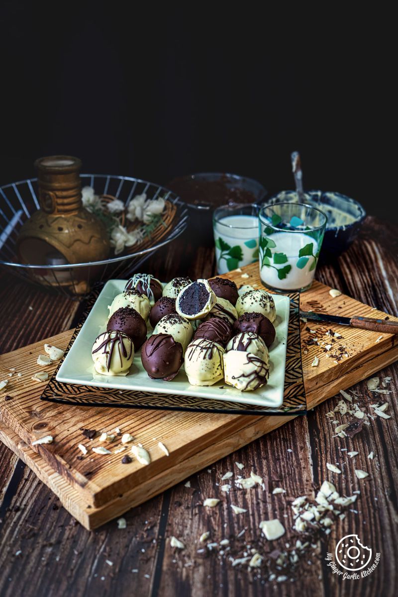 oreo truffles coated in chocolate on a yellow square plate on a wooden board with two milk glasses in the background