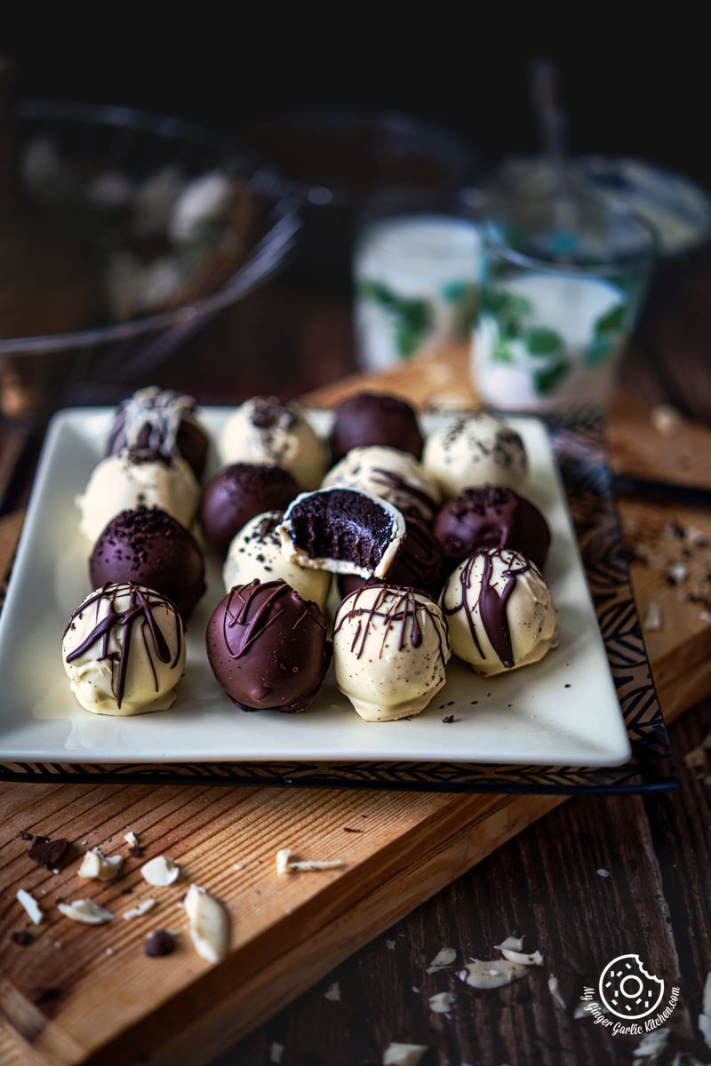 oreo truffles coated in chocolate on a yellow square plate on a wooden board with some chocolate chunks ob the side