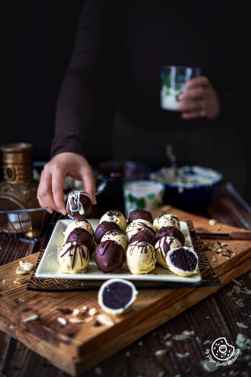 oreo truffles coated in chocolate on a yellow square plate a hand holding one truffle