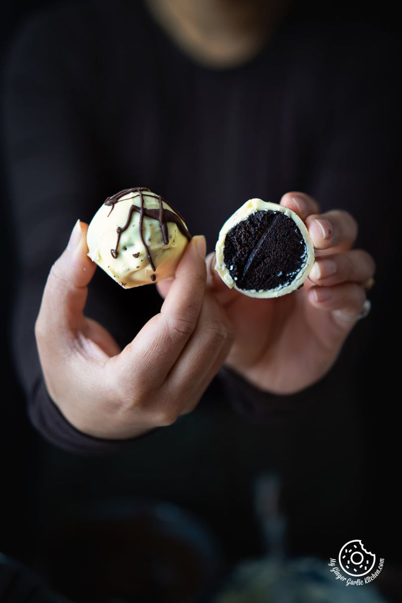 a female holding oreo half cut oreo truffle coated with white chocolate and chocolate drizzle