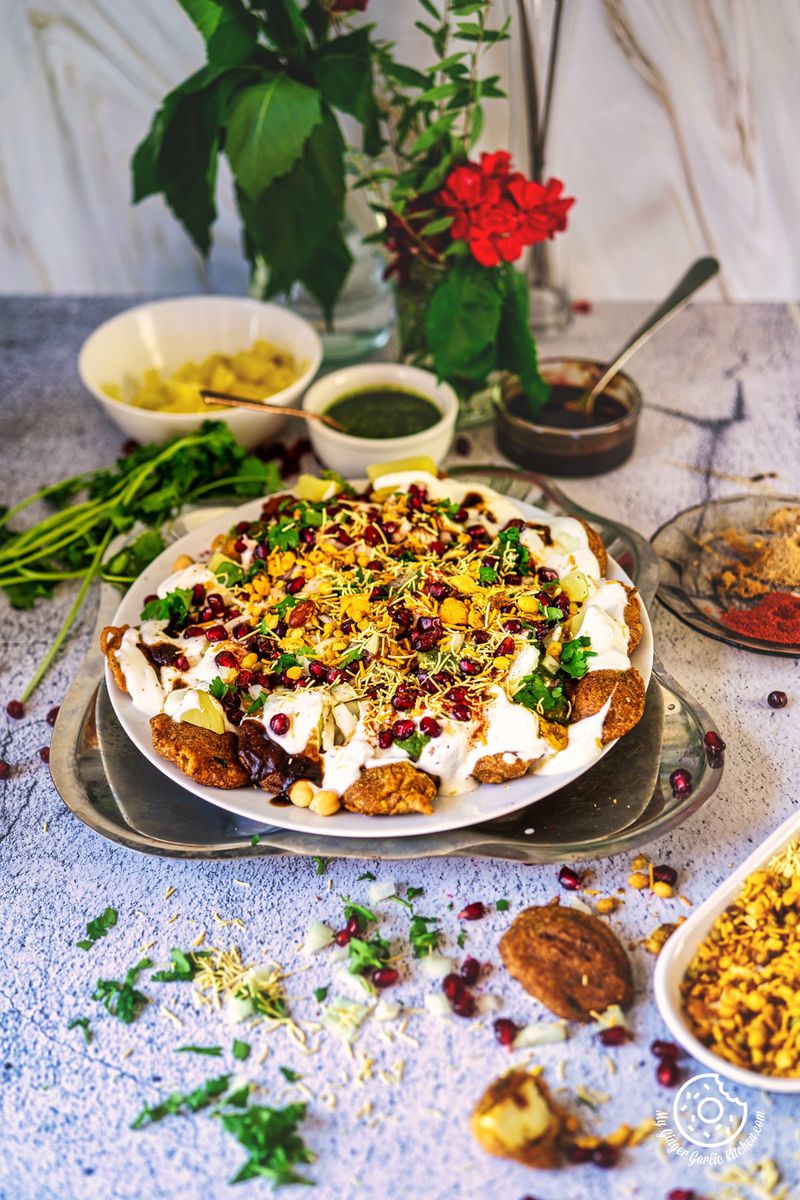 pakora chaat in a white plate with chutneys and flowers in the background