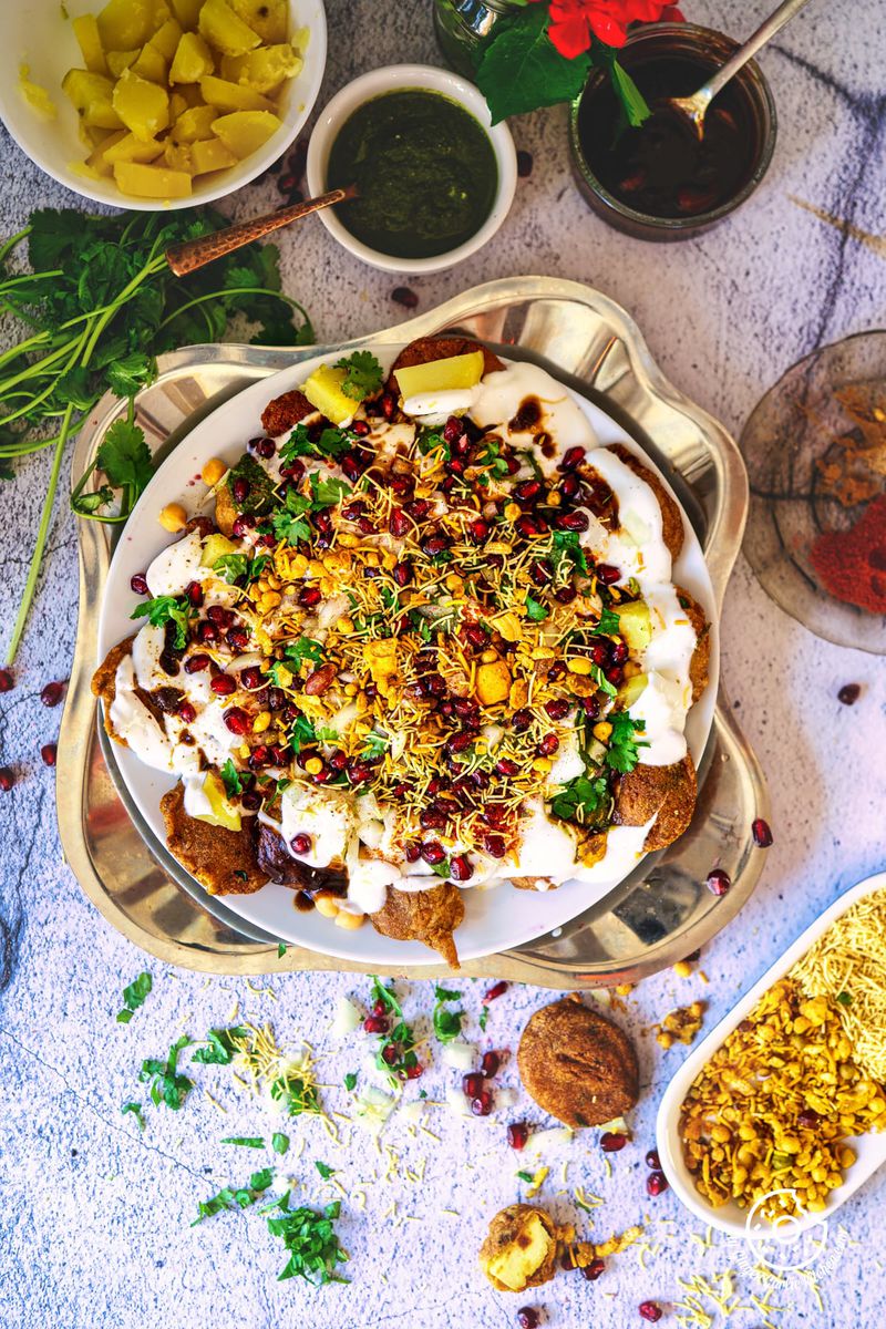 overhead shot of pakora chaat in a white plate with chutneys and flowers on the side