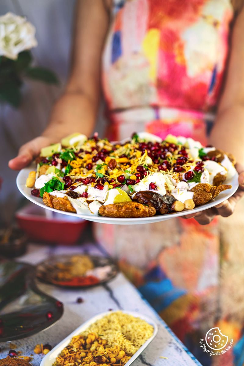 a female holding a white plate with pakora chaat