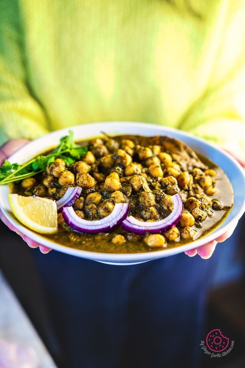 close up photo of a female holding palak chole bowl garnished with onion and cilantro
