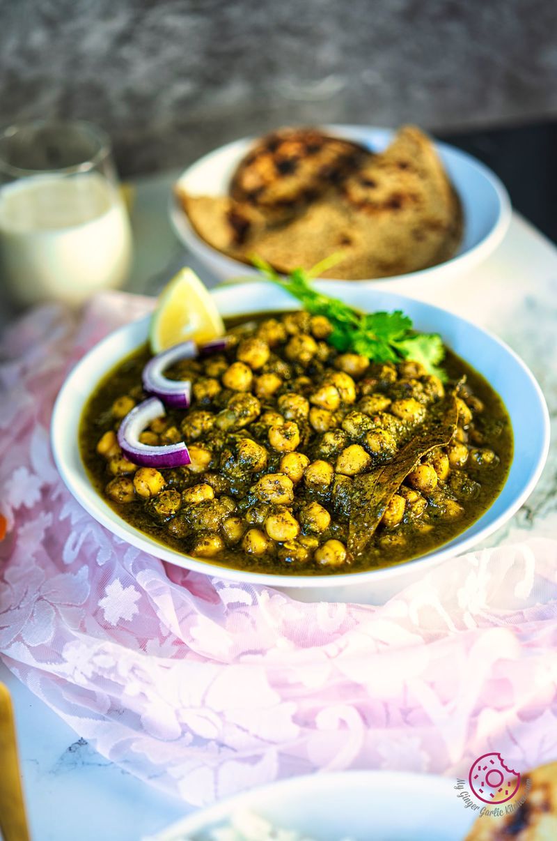 palak chole in a white bowl with a glass of buttermilk and flatbreads in the background
