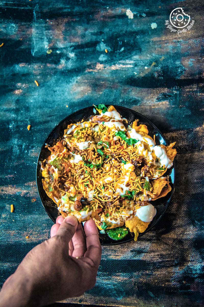 someone is holding a piece of palak patta chaat chaat over a plate of palak patta chaat with a lot of toppings