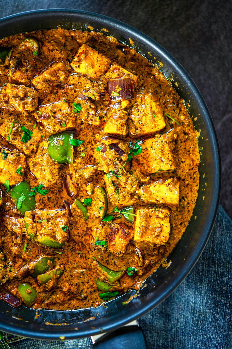 Close-up of paneer bhuna masala with golden-browned paneer, green bell peppers, and red onions in a spicy, herb-dotted masala sauce.