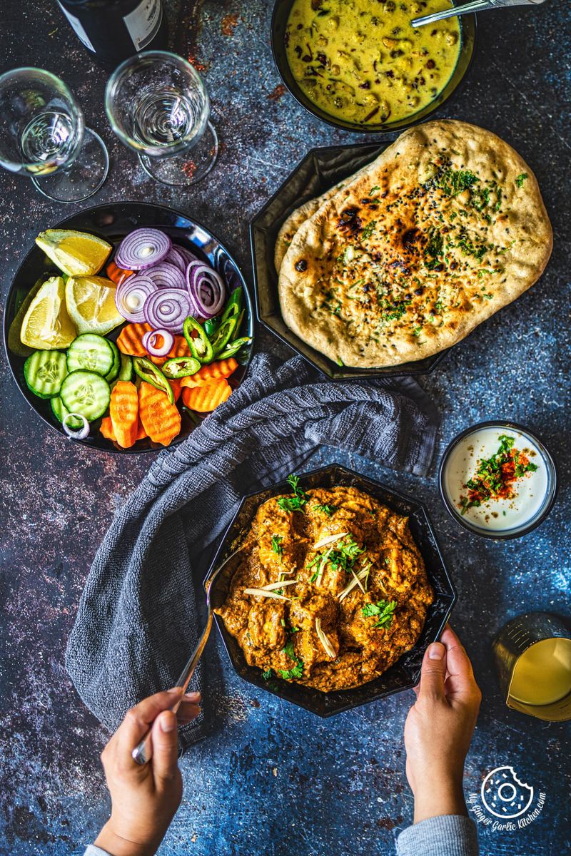 overhead shot of two hands holding paneer korma curry with some and salad on the side