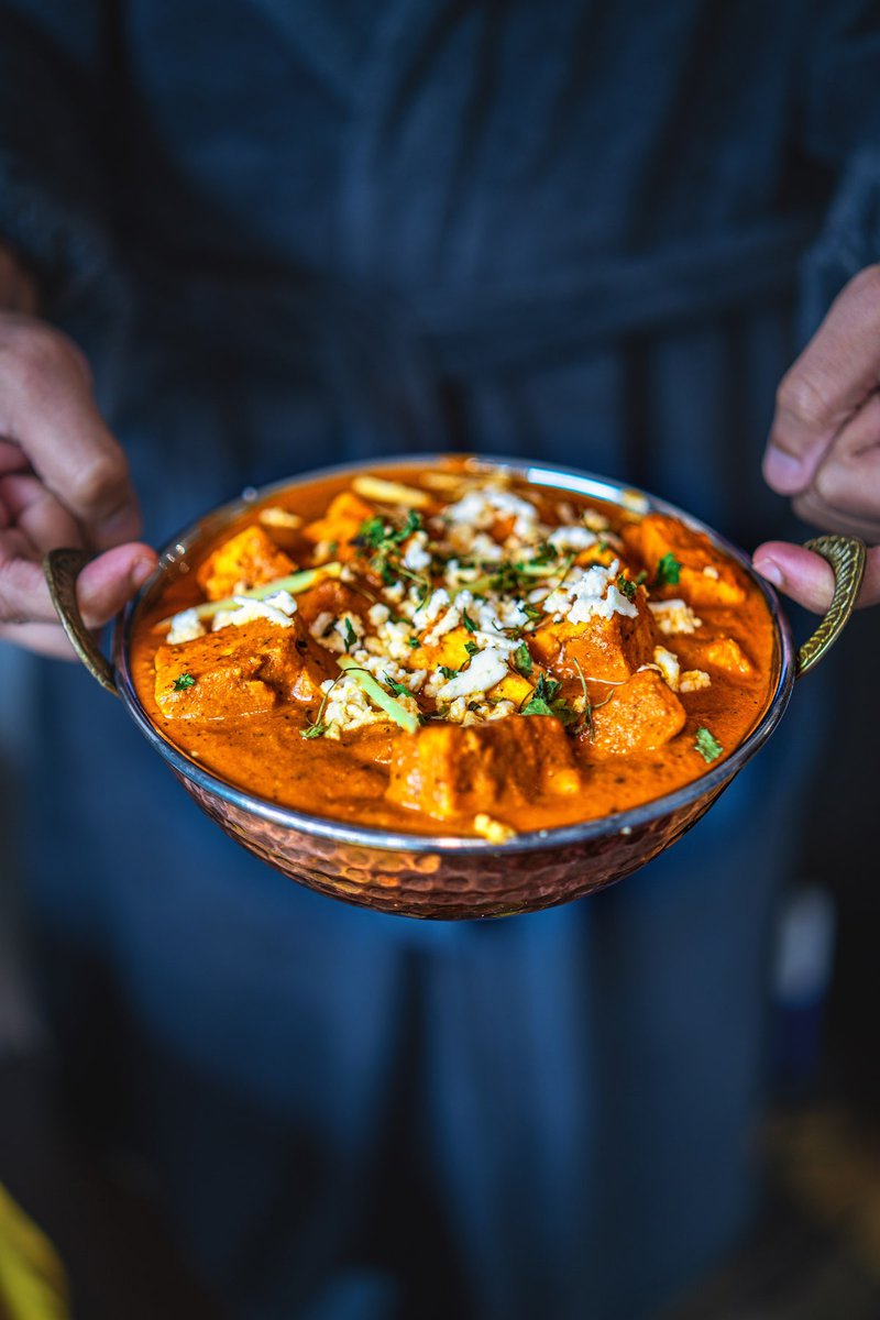 A person holding a bowl of paneer lababdar, garnished with herbs and paneer, ready to be served, showcasing the dish in a casual, inviting manner.