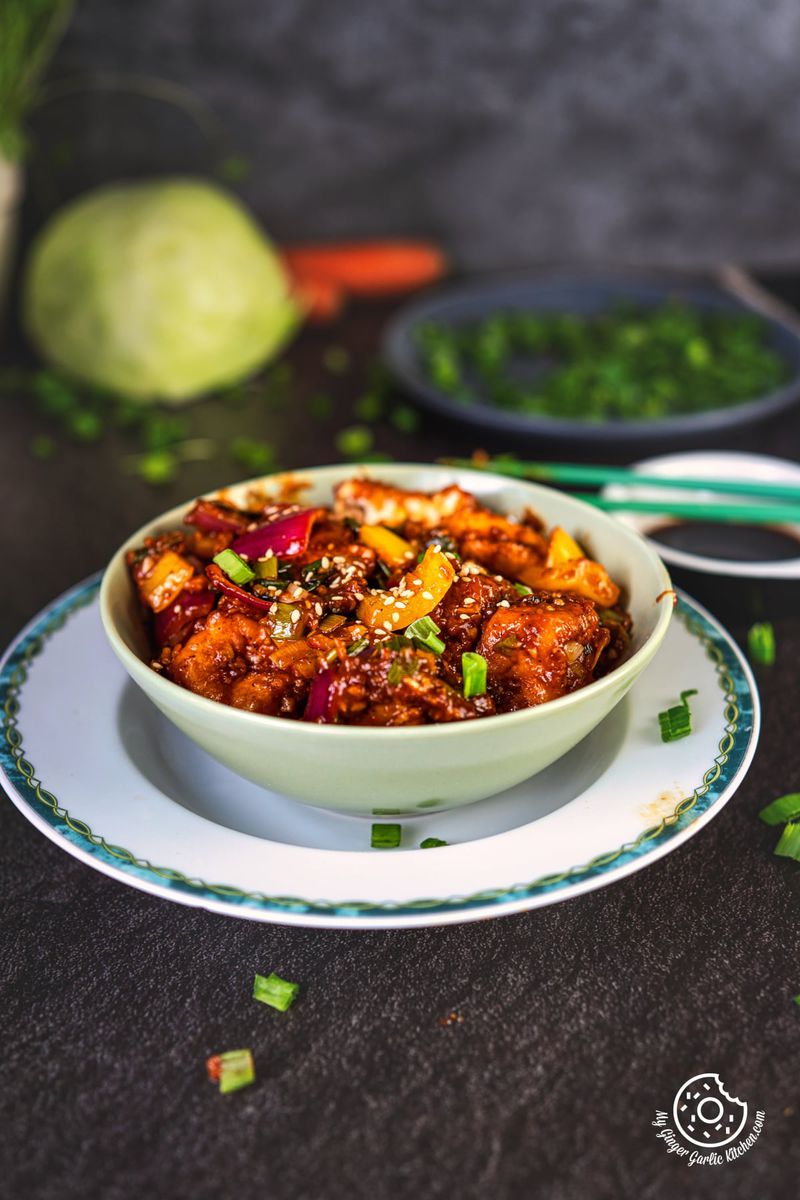 crisp fried paneer manchurian in a pale green bowl with some vegetables in the background