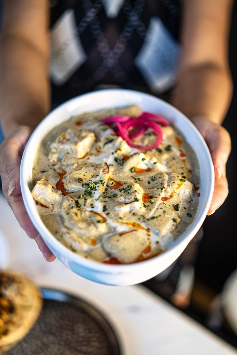 Paneer nawabi bowl held in hands, creamy white gravy paneer curry without tomato, rich and smooth texture