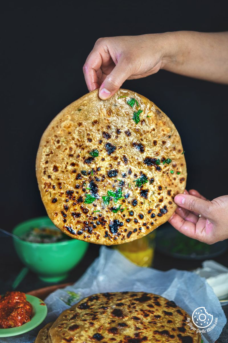 photo of a person holding a paneer paratha over a table